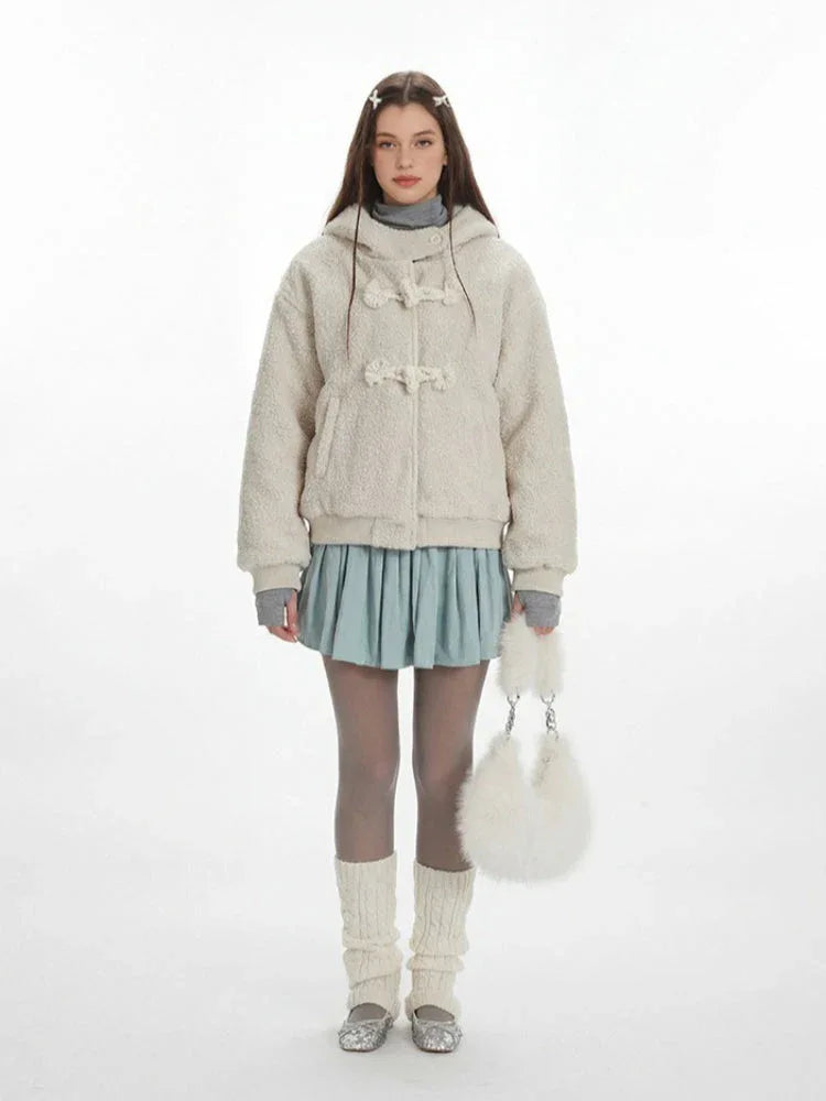 Model wearing a cream fuzzy hooded bomber jacket with toggle closure, a light blue pleated skirt, grey turtleneck, sheer tights, white leg warmers, and a white fuzzy handbag.
