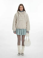 Model wearing a cream fuzzy hooded bomber jacket with toggle closure, a light blue pleated skirt, grey turtleneck, sheer tights, white leg warmers, and a white fuzzy handbag.