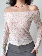 Close-up of a woman wearing a pink floral off-the-shoulder long-sleeved top with a pearl and rose necklace.