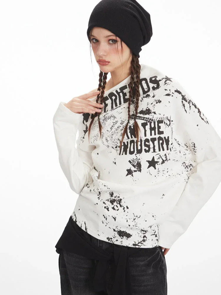 Close-up of a model wearing a white long-sleeved off-the-shoulder top with distressed graphic print, accentuating the neckline.