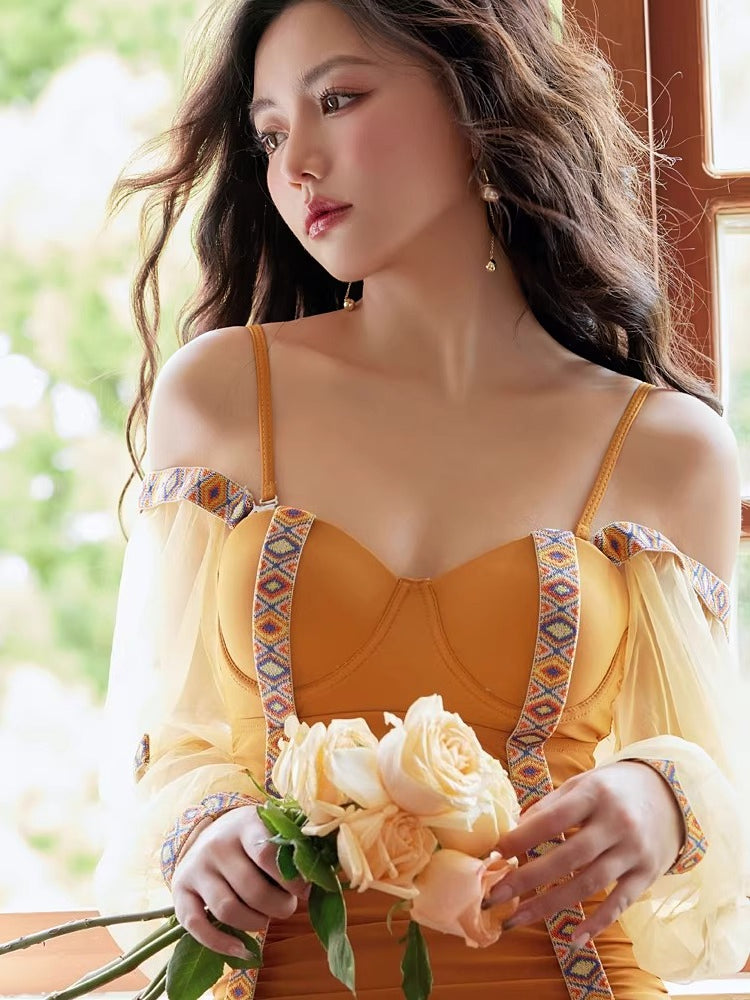 Close-up of a woman in a mustard yellow one-piece swimsuit with sheer puff sleeves and embroidered trim, holding a bouquet of roses.