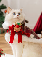 A white cat adorned in a Christmas cape featuring a reindeer character and red bows.