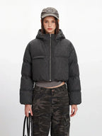 Close-up front view of a cropped grey puffer jacket with a hood and zipper closure, worn over a grey shirt and camouflage pants.