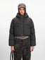 Close-up front view of a cropped grey puffer jacket with a hood and zipper closure, worn over a grey shirt and camouflage pants.