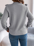 woman wearing a grey knit sweater with ruffle trim and blue jeans from the back