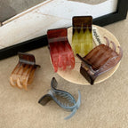 A group of four hand-shaped claw clips and one curved claw clip are arranged on a textured surface, with some clips on a small plate.