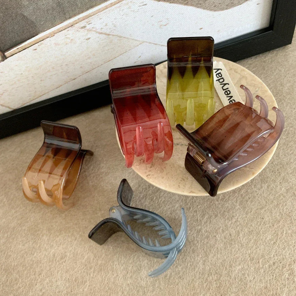 A group of four hand-shaped claw clips and one curved claw clip are arranged on a textured surface, with some clips on a small plate.