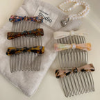 A collection of bow combs with different patterns are displayed on a beige fabric.