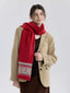 Woman wearing a red knit scarf with a Fair Isle pattern on the ends, over a tan blazer and brown dress.