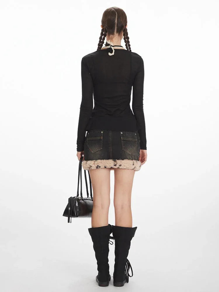 Back view of a woman wearing a black long-sleeved top, denim mini skirt with fur trim, and black knee-high boots, holding a black shoulder bag.