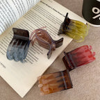 Several hand-shaped claw clips are scattered on top of a book, showcasing different colors like brown, green, red, and blue-grey.