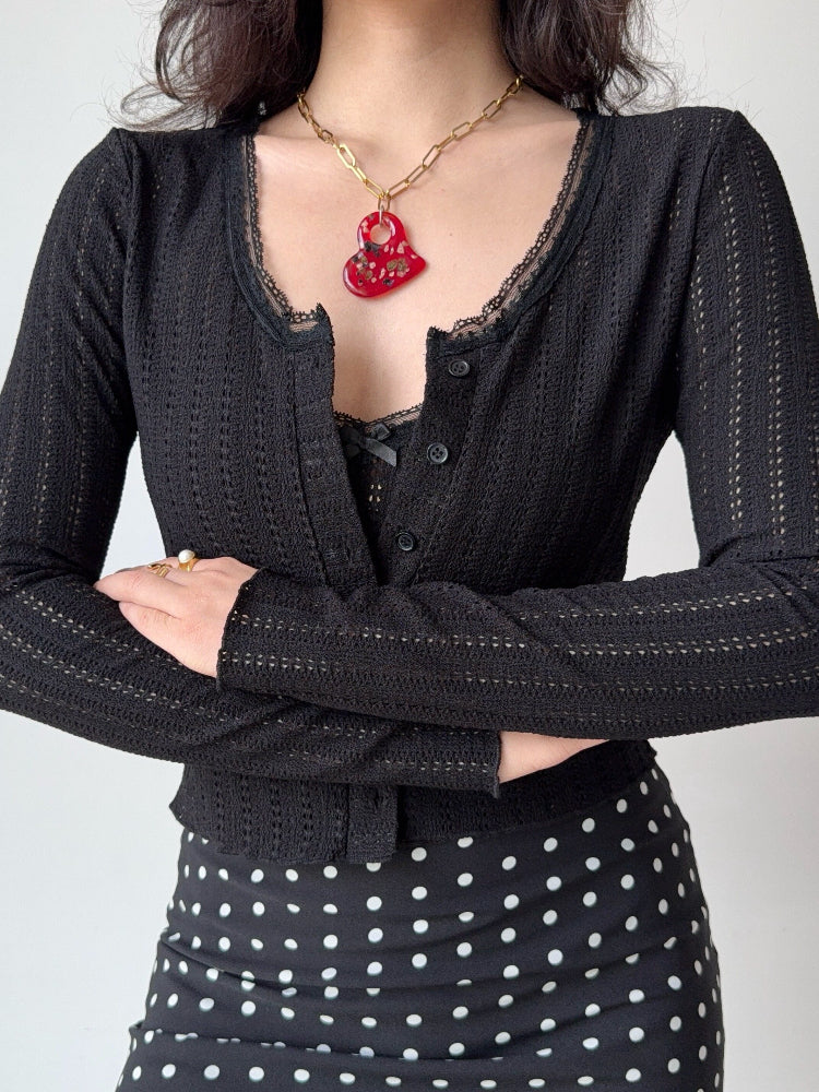 Woman wearing a black cropped knit cardigan with lace trim and a black polka dot skirt.