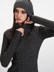 Close-up view of a model adjusting the zipper on a gray striped long-sleeve top with a mock neck and thumbholes.
