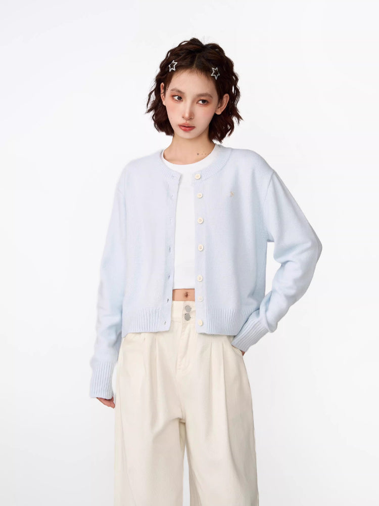 Side view of a woman in a light blue cropped knit cardigan, white crop top, and cream wide-leg pants.