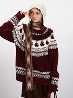 Woman adjusting her white beanie while wearing a maroon and white knit sweater with an apple Fair Isle pattern and a patterned scarf.