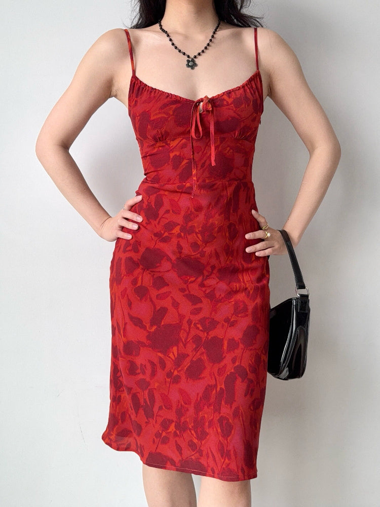 Model wearing a red floral print midi dress with adjustable spaghetti straps and a tie front detail.
