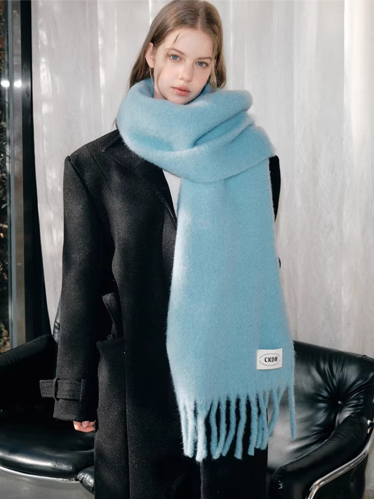 Woman posing with a light blue fluffy knit scarf and a black coat.