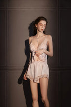 Woman with eyes closed, wearing a cream satin camisole and shorts set with pink lace trim.
