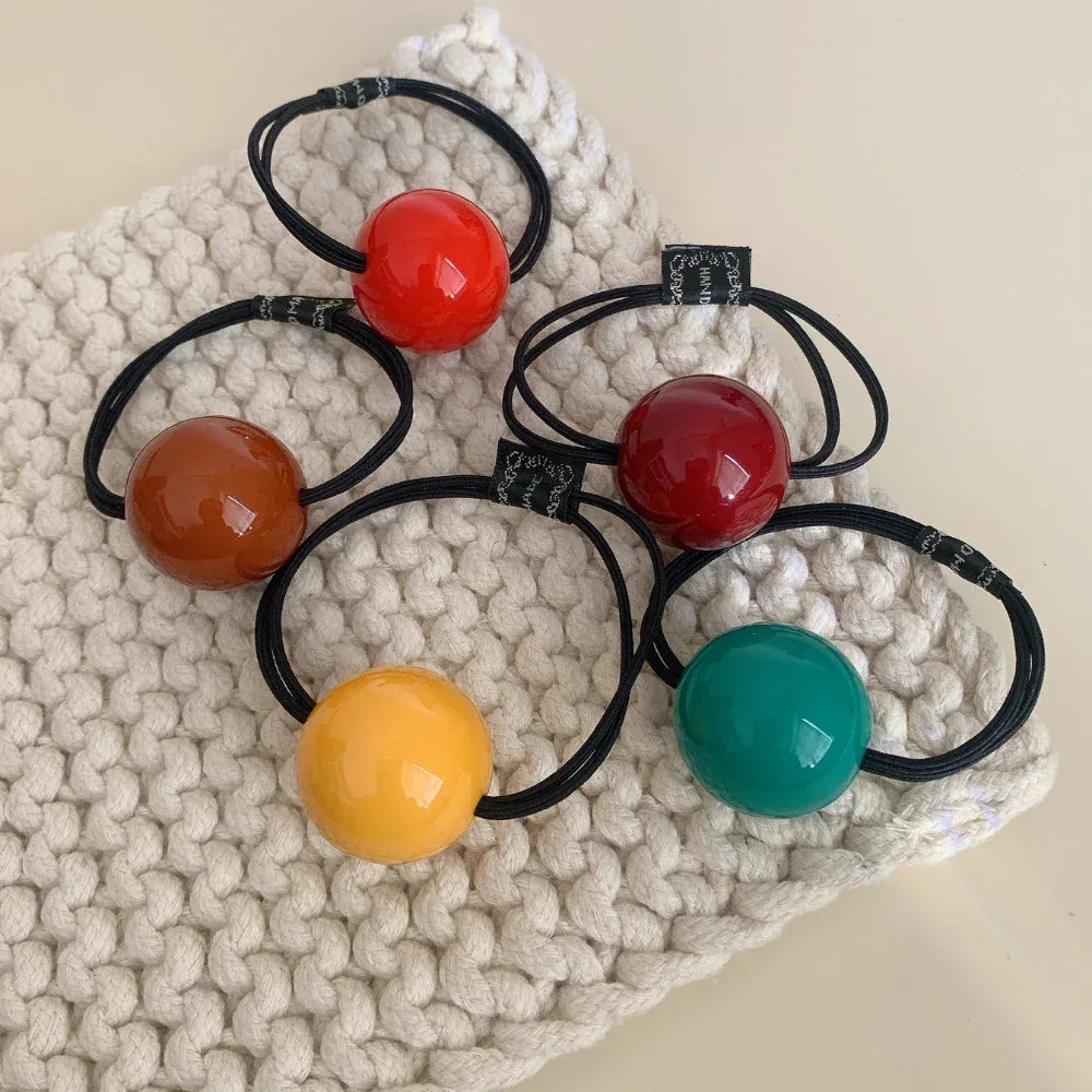 Five colorful ball hair ties on a white textured surface