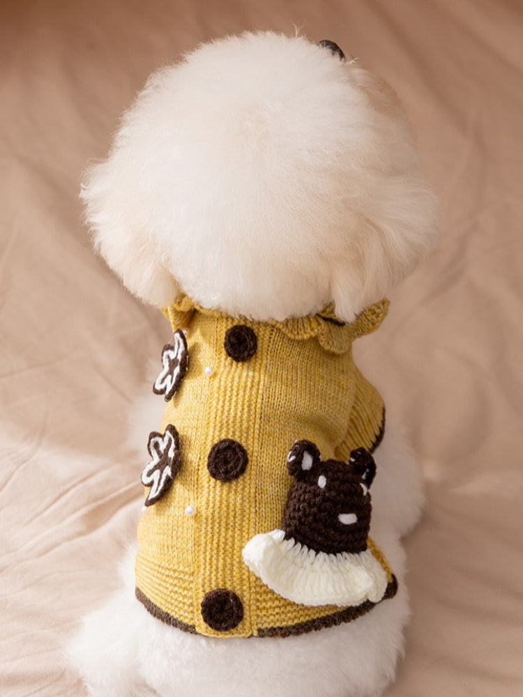 The back of a white bichon frise dog wearing a yellow knitted sweater with floral appliques and a bear detail.