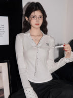 Woman wearing a white ribbed long-sleeve shirt with polka dot accents and a tie detail at the neckline.