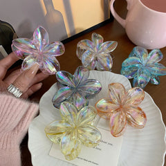 hand holding an iridescent flower claw hair clip with other clips in the background