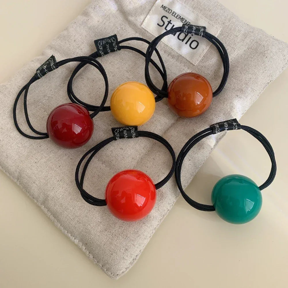 Five colorful ball hair ties on a light fabric surface
