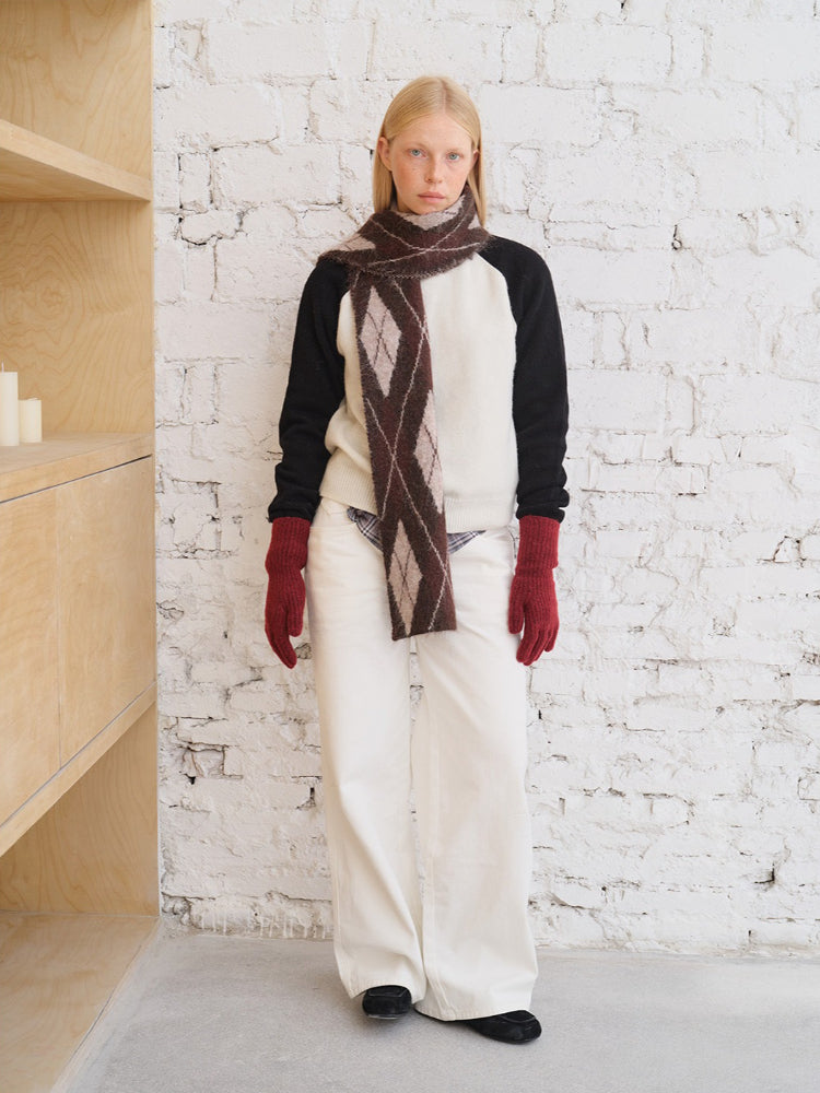 Model wearing a cream and black sweater with an argyle scarf and white pants