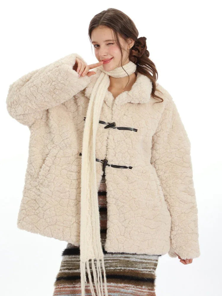 Close-up of a woman wearing a cream-colored fleece coat with toggle closures and a cream scarf, winking and holding up a finger.
