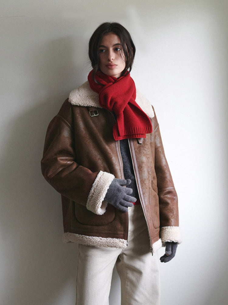 A woman wearing a brown aviator jacket, red scarf, and grey gloves.