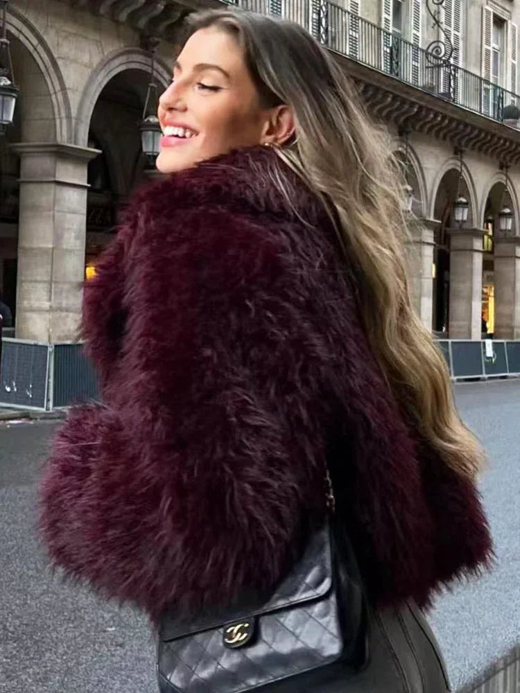 Woman wearing a burgundy shaggy faux fur cropped jacket and a black quilted handbag.