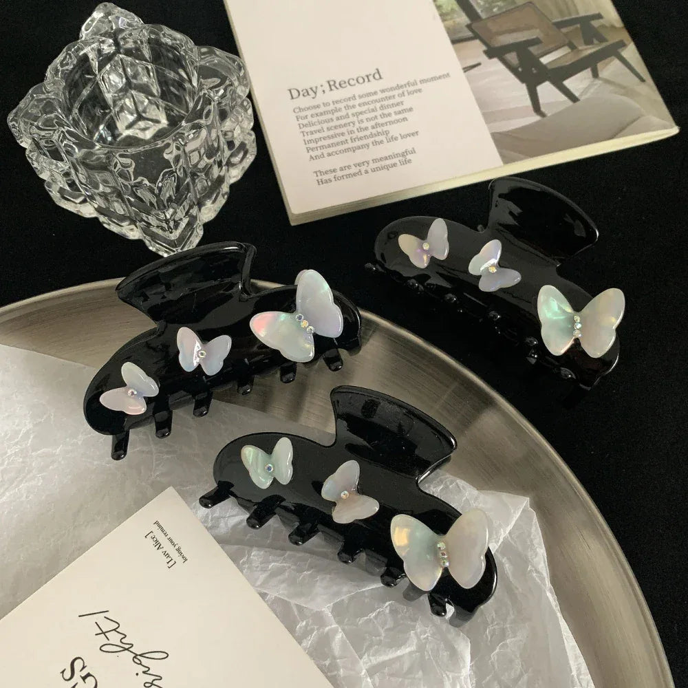 Three black claw clips with iridescent butterfly embellishments arranged on a silver tray
