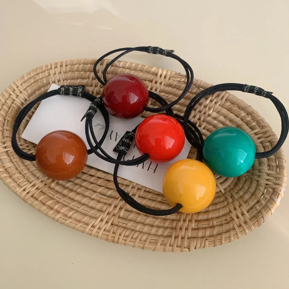 Five colorful ball hair ties on a wicker tray