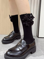 View of black knee-high socks with flower accents and shiny black loafers.