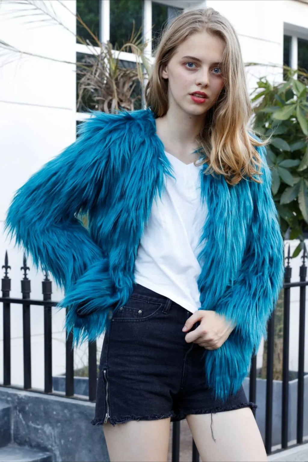 Woman posing in a teal faux fur jacket and black shorts