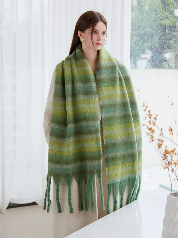 A woman stands indoors, wearing a cream coat and a green striped scarf, showcasing the fringe detail.