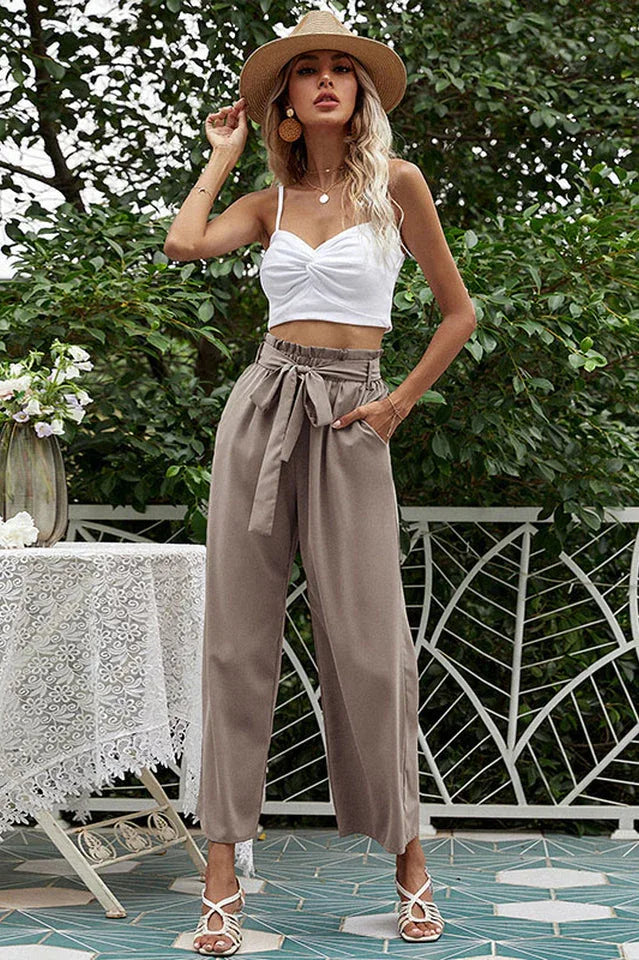 Woman wearing a white crop top and taupe wide-leg pants with a tie belt, wearing a straw hat.