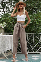 Woman wearing a white crop top and taupe wide-leg pants with a tie belt, wearing a straw hat.