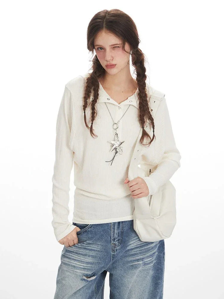 Close-up of a woman wearing a white ribbed knit long-sleeve shirt with a star pendant necklace and distressed wide-leg blue jeans, holding a white handbag.