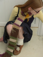 Close-up of a woman's lower body showing a denim skirt, white socks, brown shoes, and a portion of a fuzzy striped scarf.