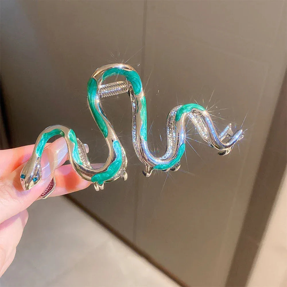 Hand holding a snake-shaped hair clip with green and silver enamel.