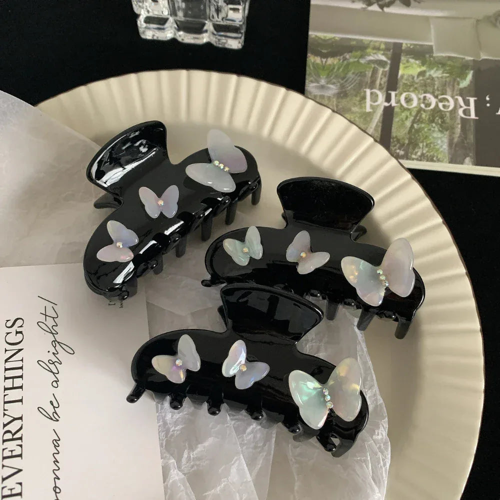 Close-up of black claw clips with iridescent butterfly embellishments on a white textured paper