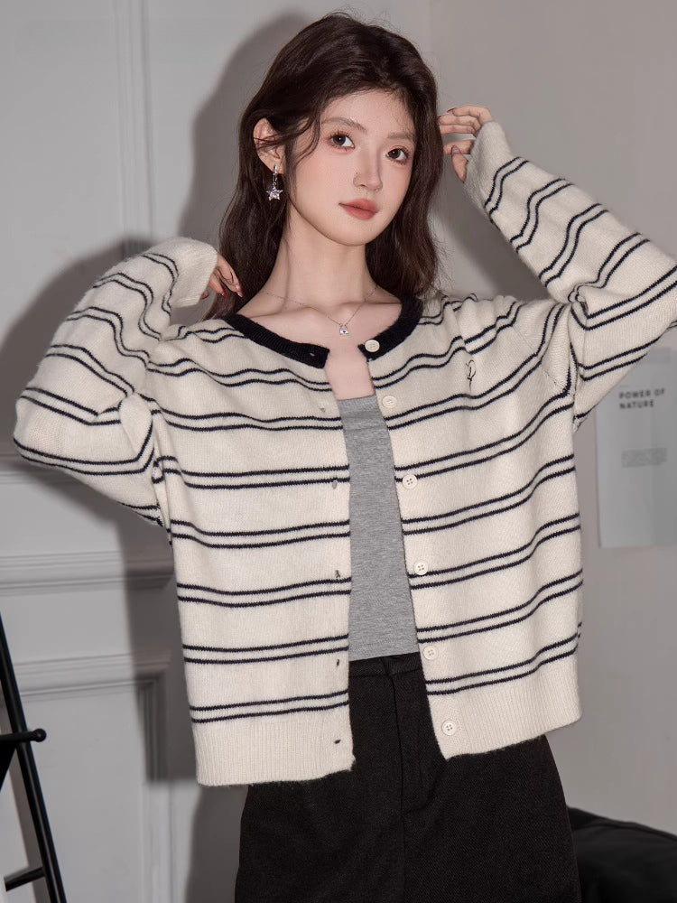 Woman wearing a cream and black striped button-up knit cardigan layered over a grey tank top.