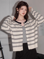 Woman wearing a cream and black striped button-up knit cardigan layered over a grey tank top.