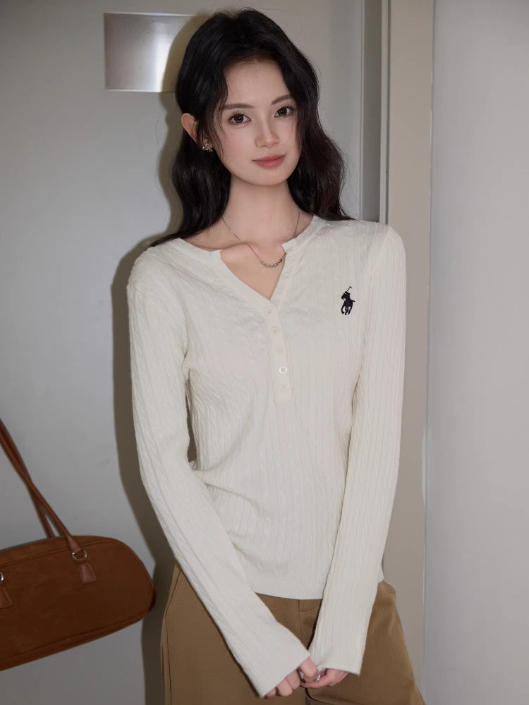 Close-up of a woman's torso showing the white cable knit henley sweater with a black embroidered logo.
