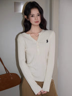 Close-up of a woman's torso showing the white cable knit henley sweater with a black embroidered logo.