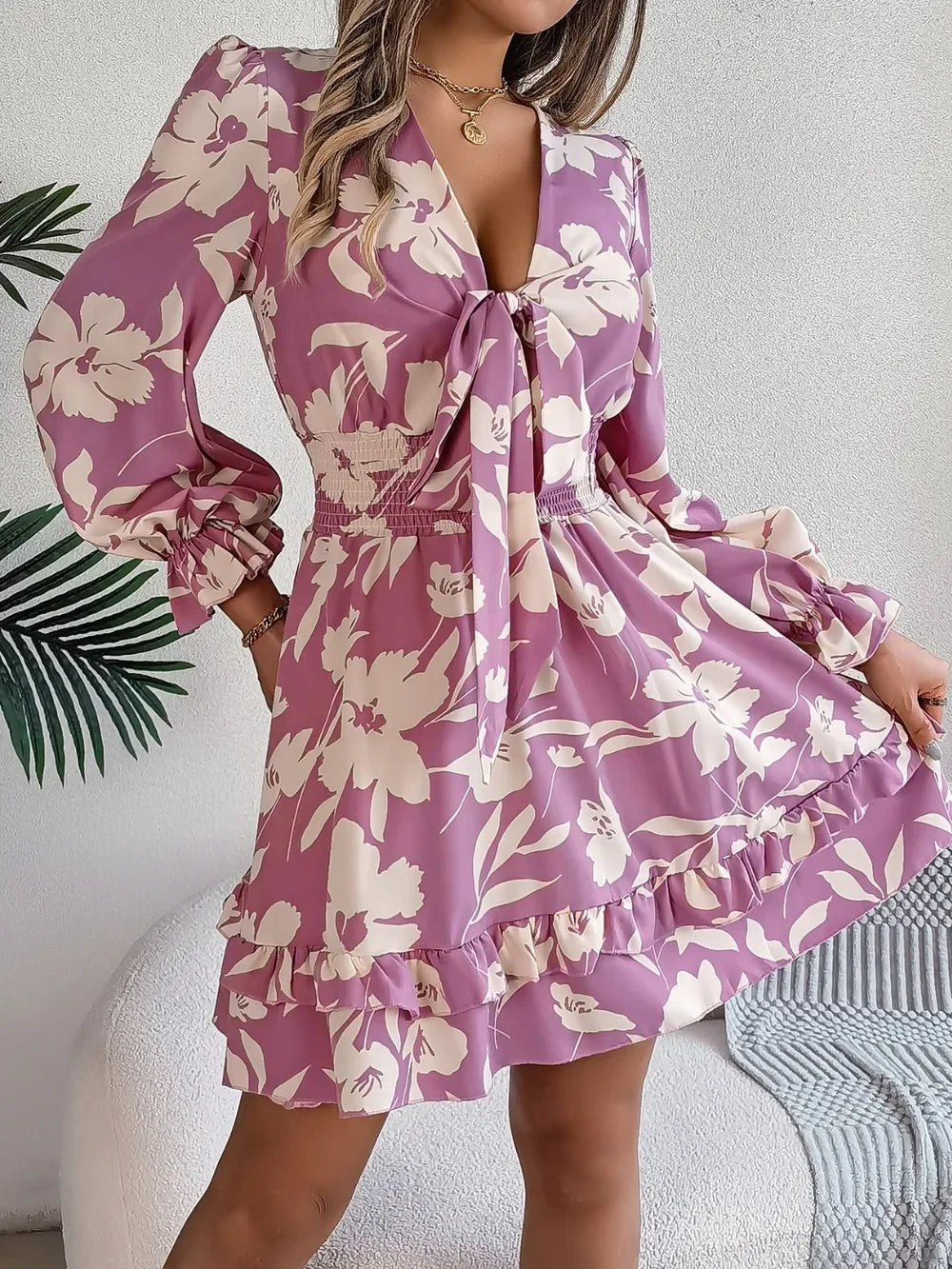 woman standing and holding a straw bag, wearing a purple floral print mini dress