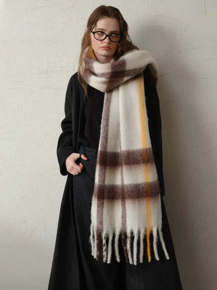 Woman wearing a long dark coat and a large plaid scarf with white, brown, and yellow stripes.