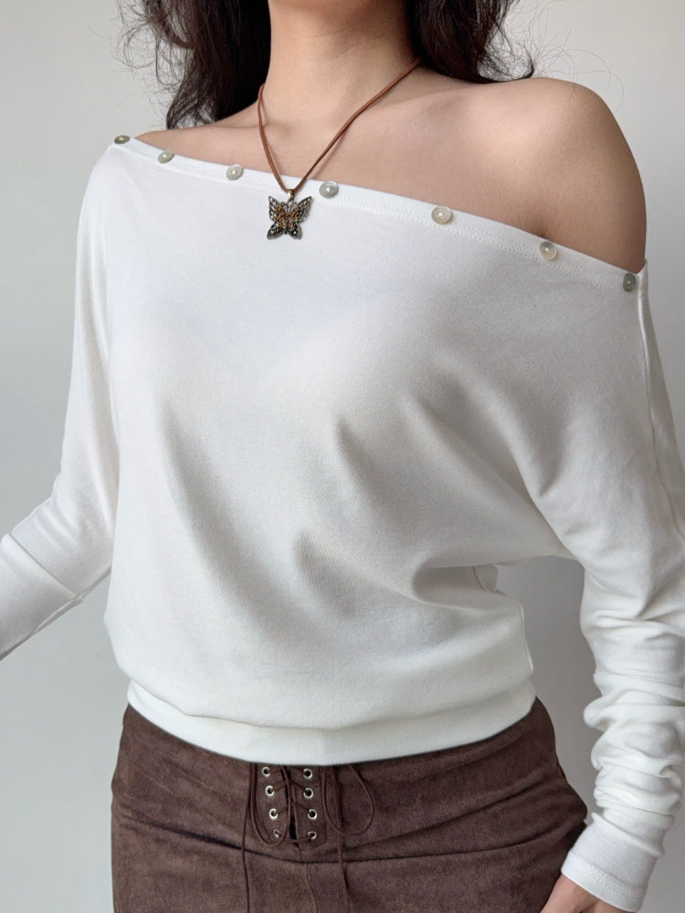 Close-up of a white off-the-shoulder knit top with decorative buttons.