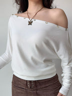 Close-up of a white off-the-shoulder knit top with decorative buttons.
